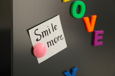 Photo of Note with phrase SMILE MORE and magnets on refrigerator, closeup