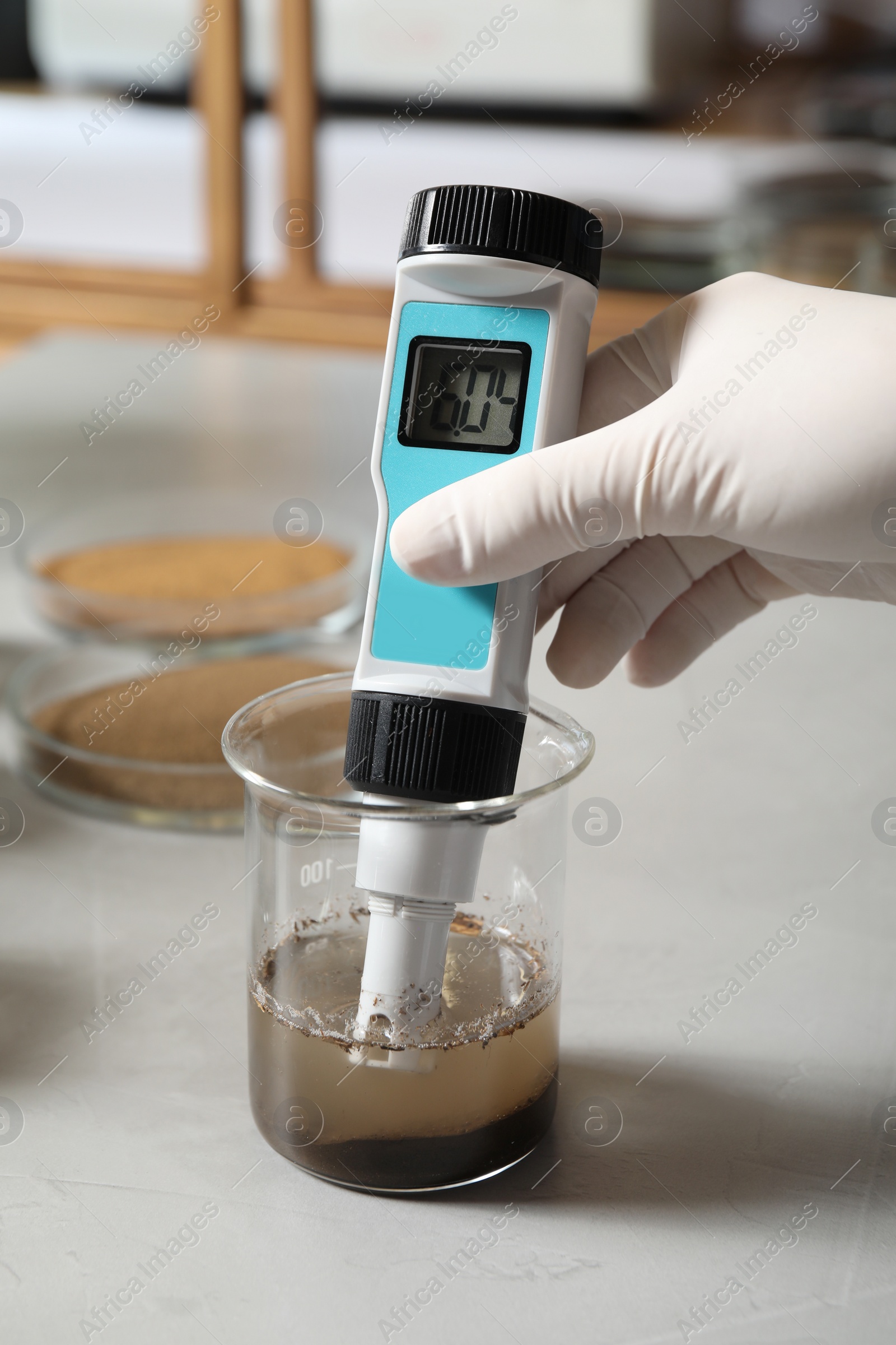 Photo of Scientist measuring acidity and pH of soil at table, closeup. Laboratory analysis