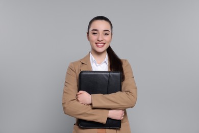 Photo of Happy real estate agent with leather portfolio on grey background