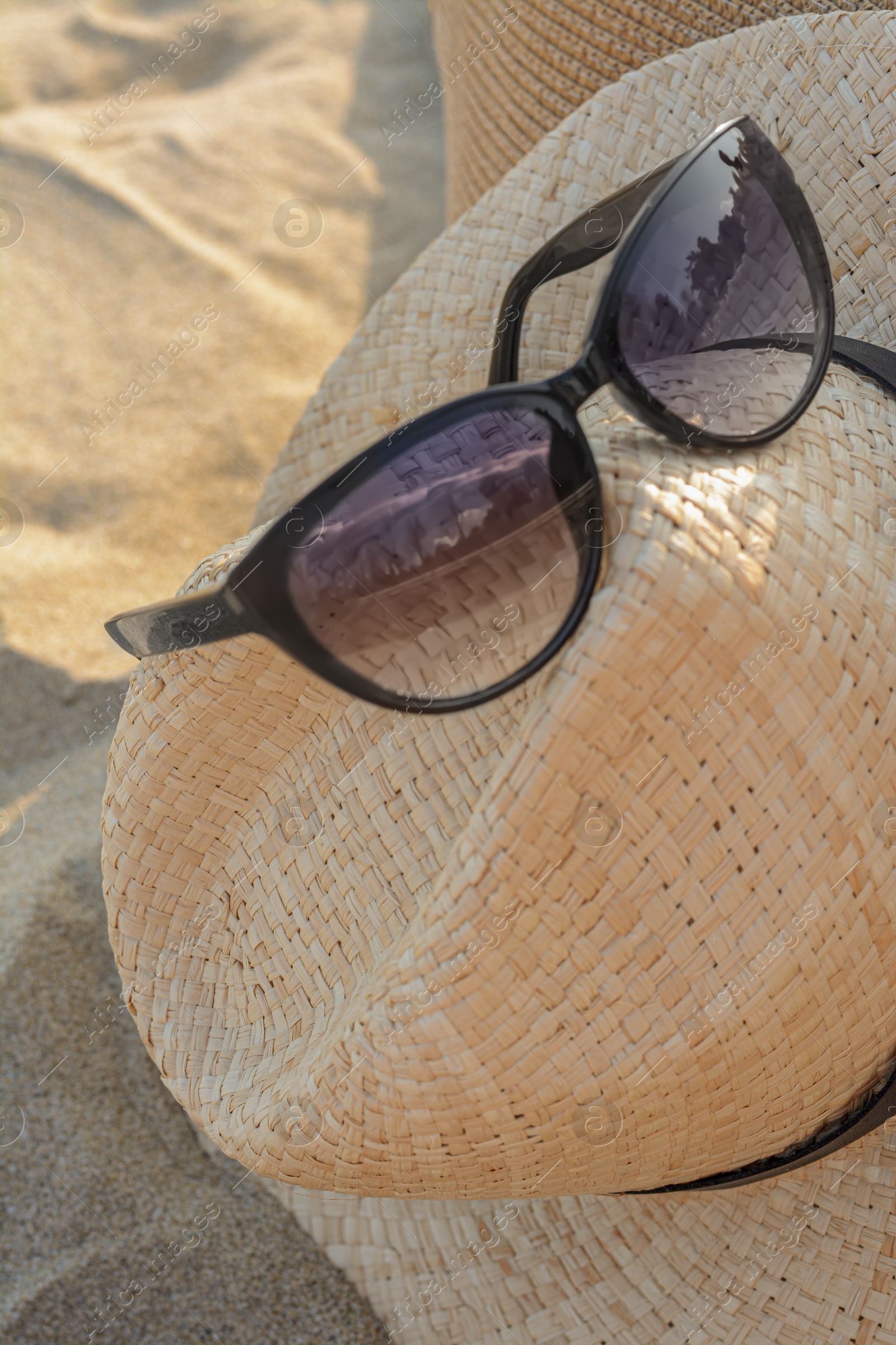 Photo of Hat with beautiful sunglasses on sandy beach, closeup