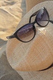 Photo of Hat with beautiful sunglasses on sandy beach, closeup