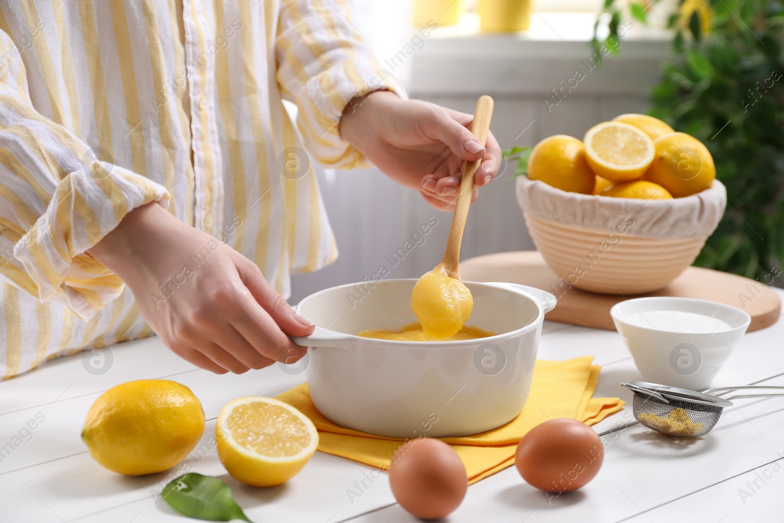 Photo of Woman cooking lemon curd at white wooden table, closeup