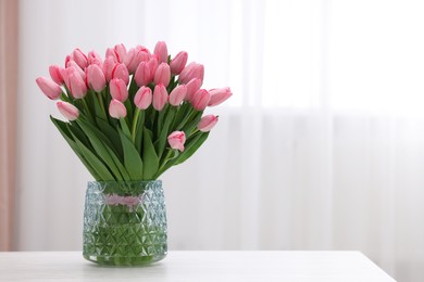 Photo of Bouquet of beautiful pink tulips in vase on white wooden table indoors, space for text