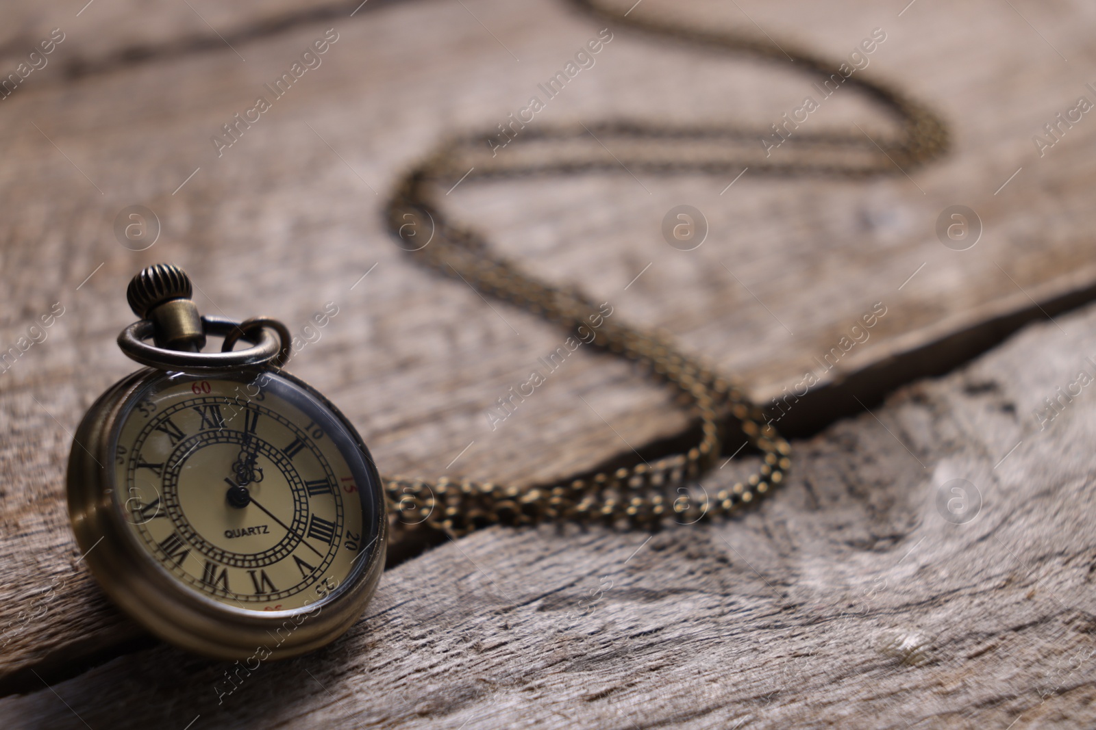 Photo of Pocket clock with chain on wooden table, closeup. Space for text