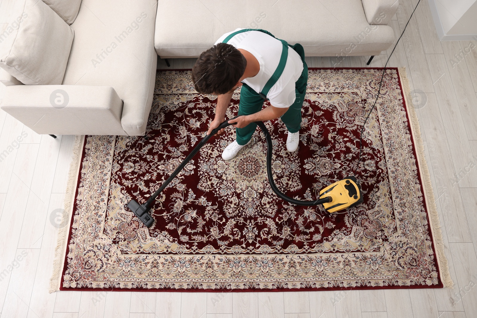 Photo of Dry cleaner's employee hoovering carpet with vacuum cleaner indoors, above view