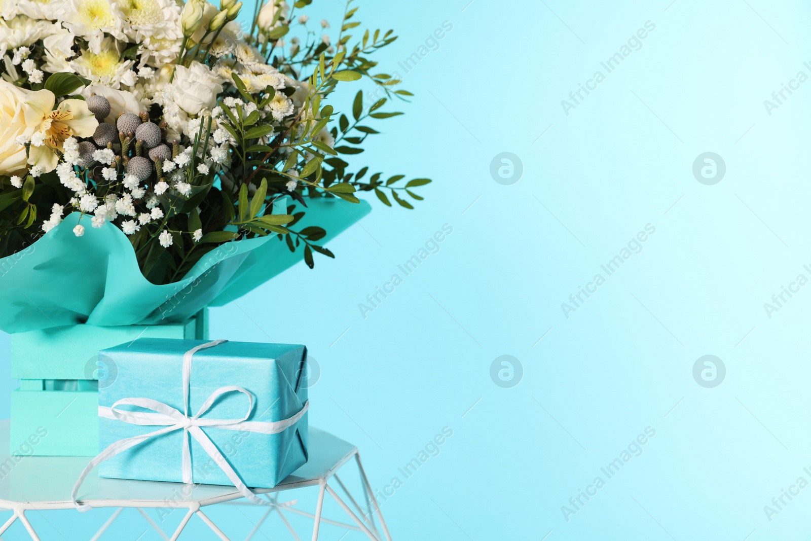 Photo of Beautiful bouquet of flowers and gift box on table against color background. Space for text