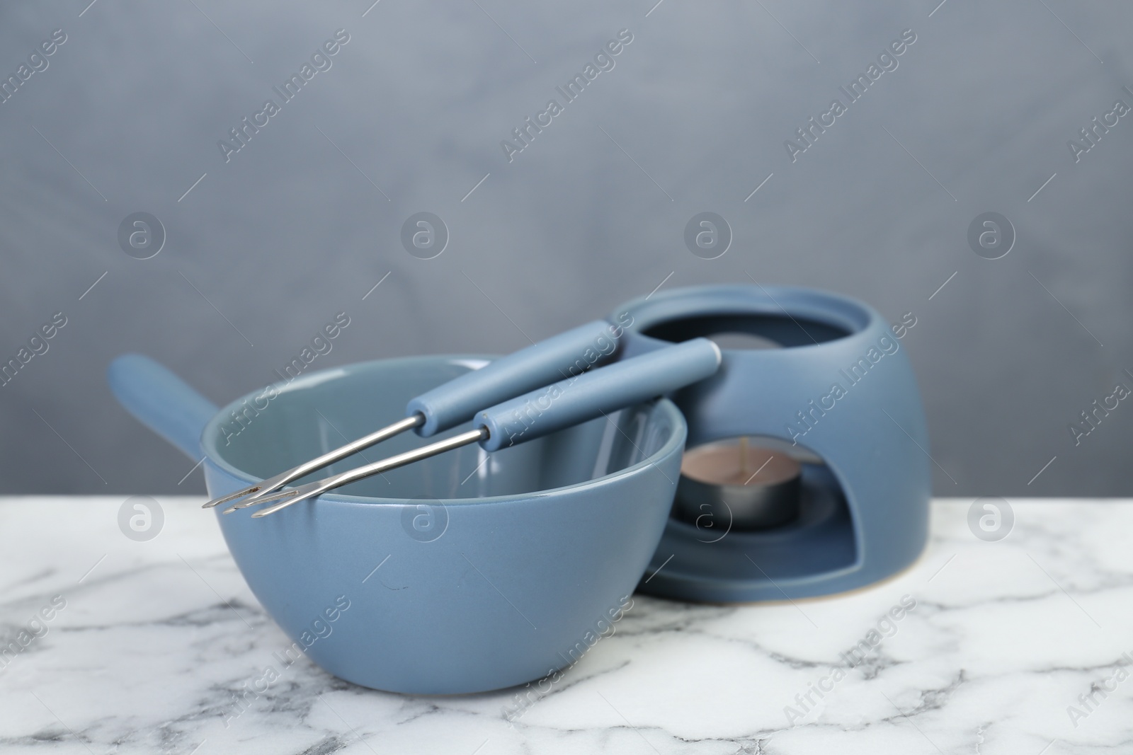 Photo of Fondue set on white marble table against light gray wall
