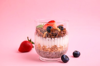 Photo of Tasty granola with berries, nuts, yogurt and chia seeds in glass on pink background