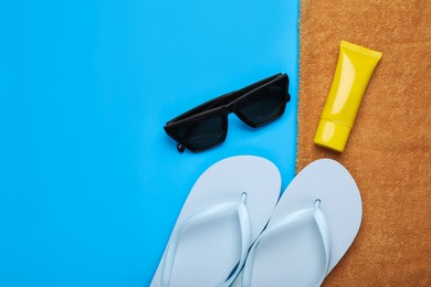 Photo of Flip flops, sunscreen, sunglasses and towel on light blue background, flat lay. Space for text
