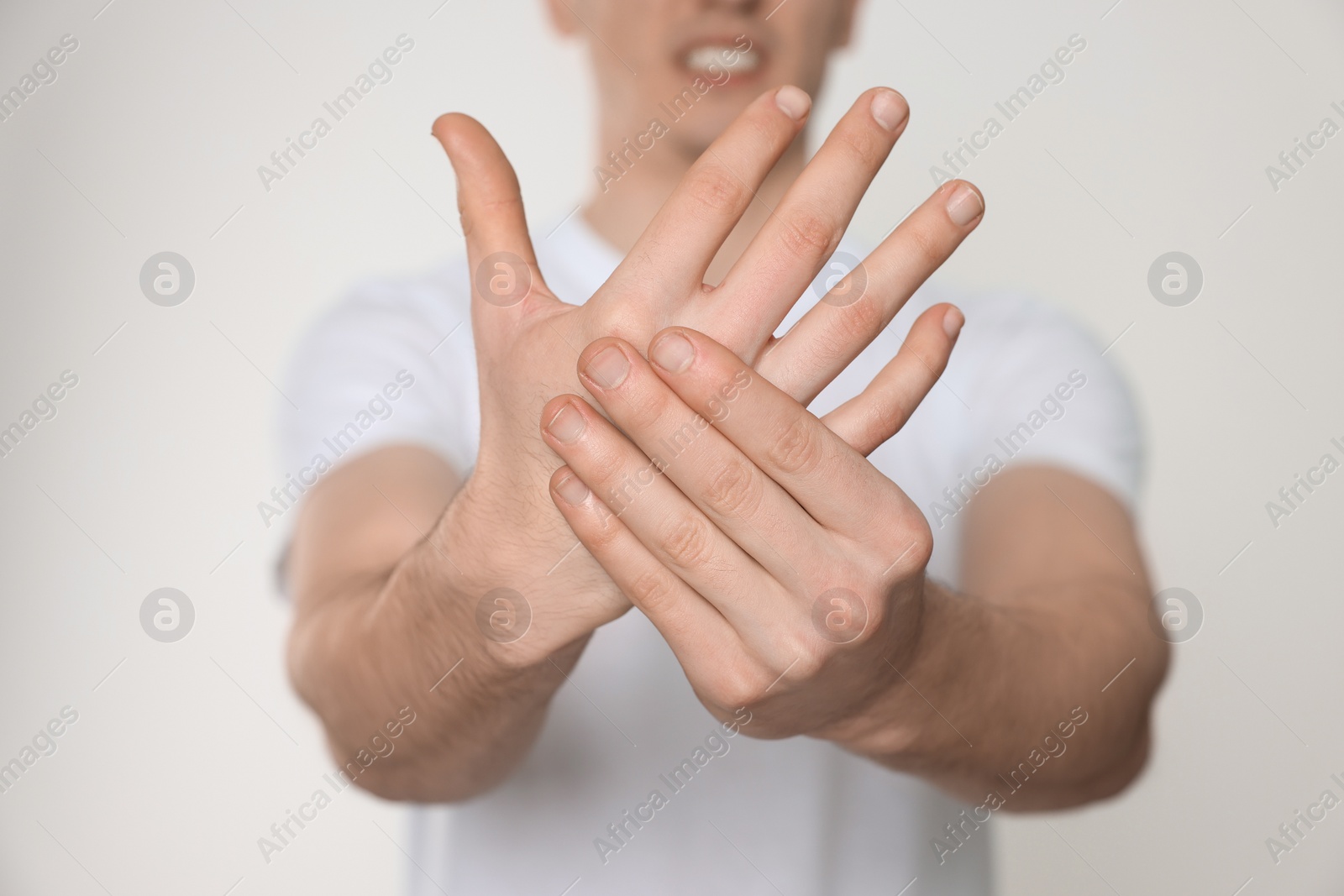 Photo of Man suffering from pain in his hand on light background, closeup. Arthritis symptoms