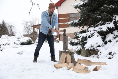 Photo of Man chopping wood with axe outdoors on winter day