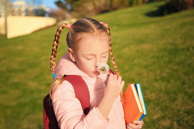 Cute little girl with dandelion, backpack and textbooks outdoors