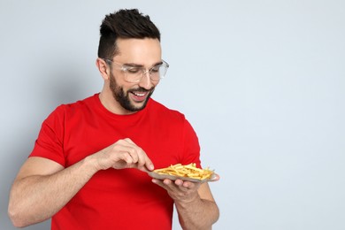 Man with French fries on grey background, space for text