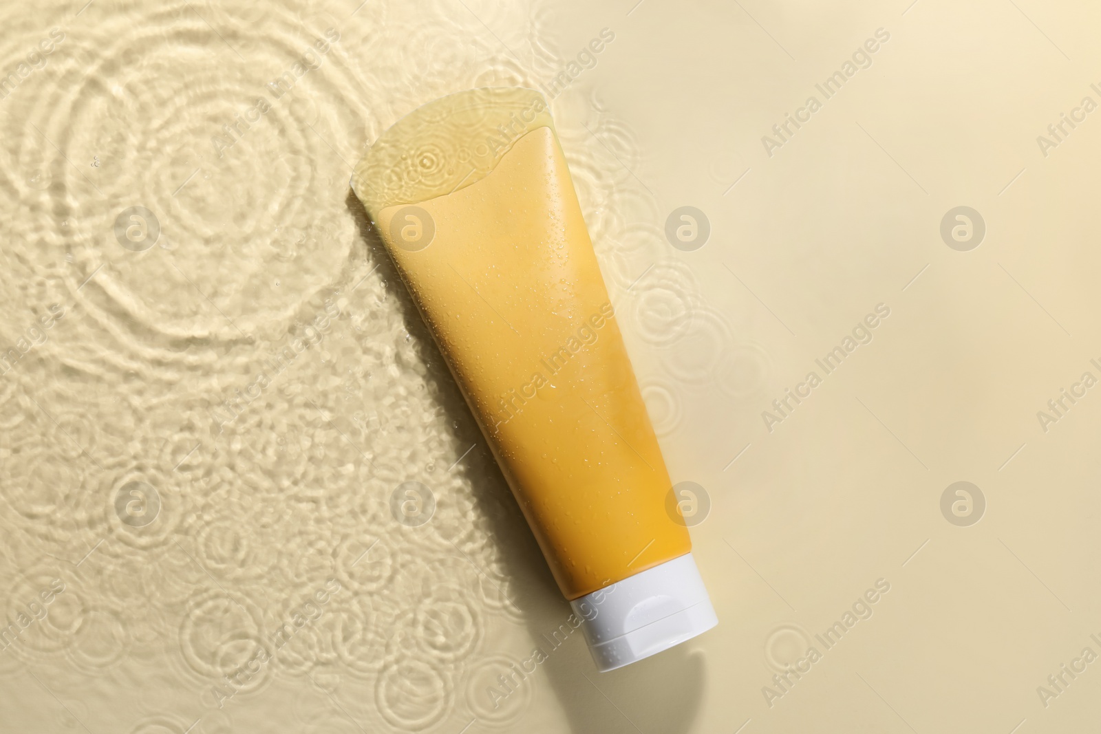 Photo of Tube of face cleansing product in water against beige background, top view