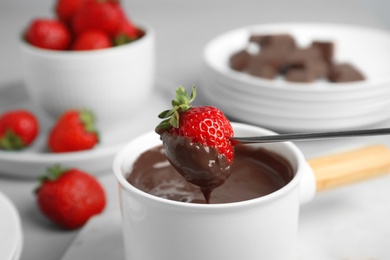 Photo of Dipping strawberry into fondue pot with chocolate on grey table, closeup