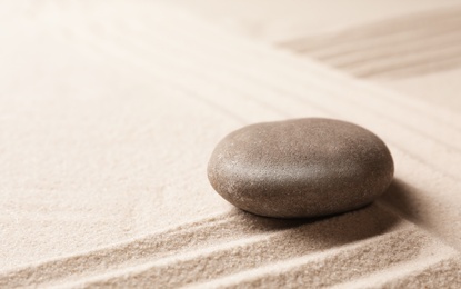 Zen garden stone on sand with pattern, space for text. Meditation and harmony