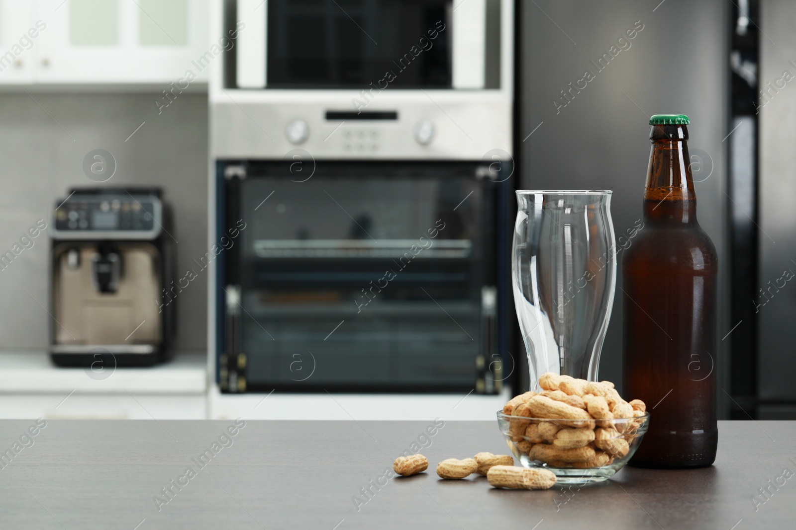 Photo of Glass, bottle of beer and bowl with peanuts on grey table in kitchen. Space for text