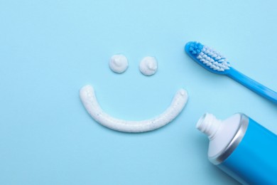 Photo of Funny face made with toothpaste, brush and tube on light blue background, flat lay