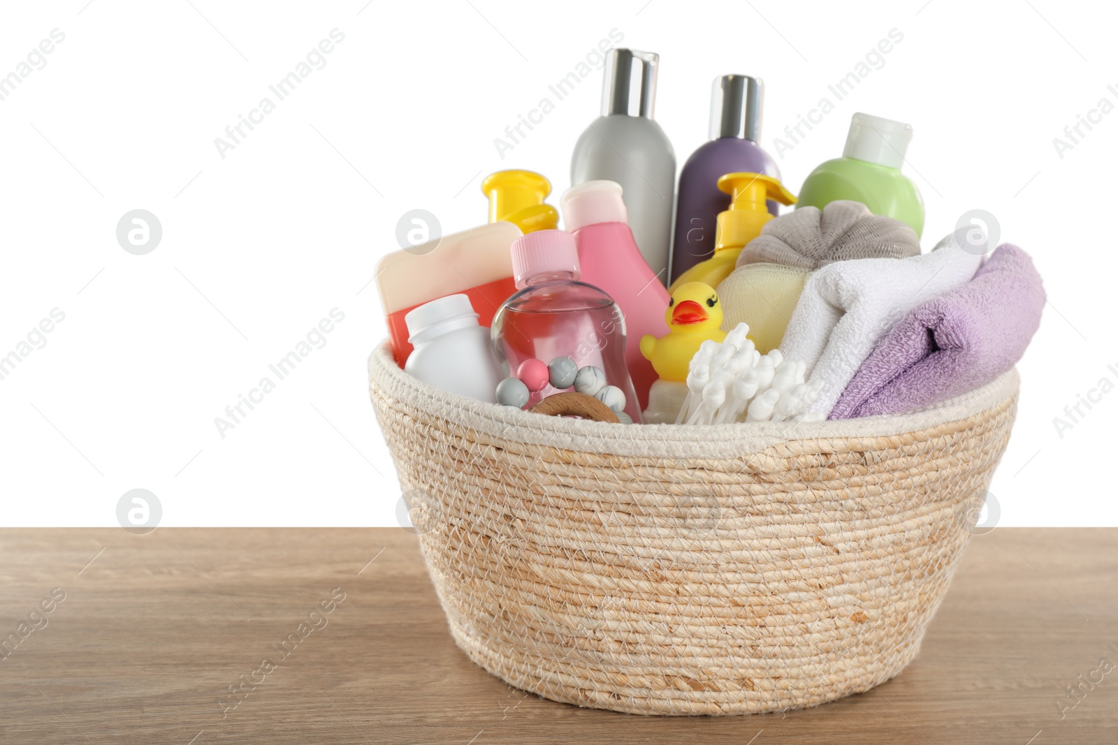 Photo of Wicker basket full of different baby cosmetic products, bathing accessories and toys on wooden table against white background