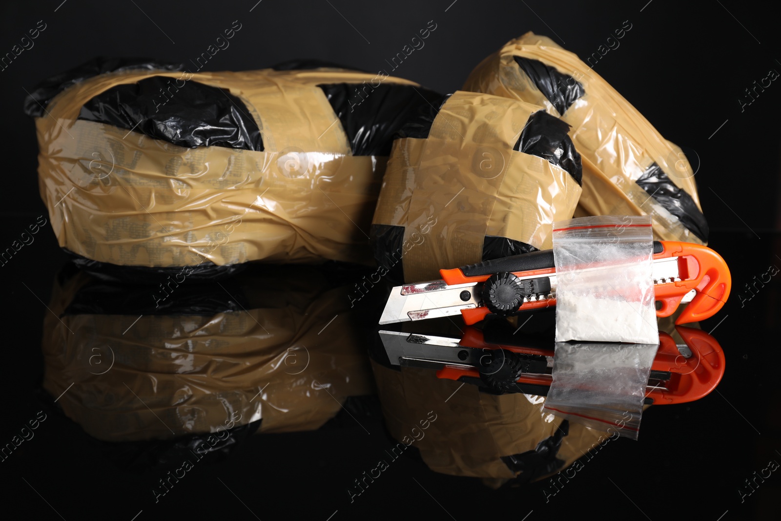 Photo of Smuggling, drug trafficking. Packages with narcotics and utility knife on black mirror surface