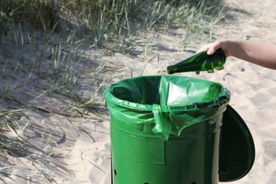 Photo of Woman throwing glass bottle in bin on beach, closeup. Recycling concept