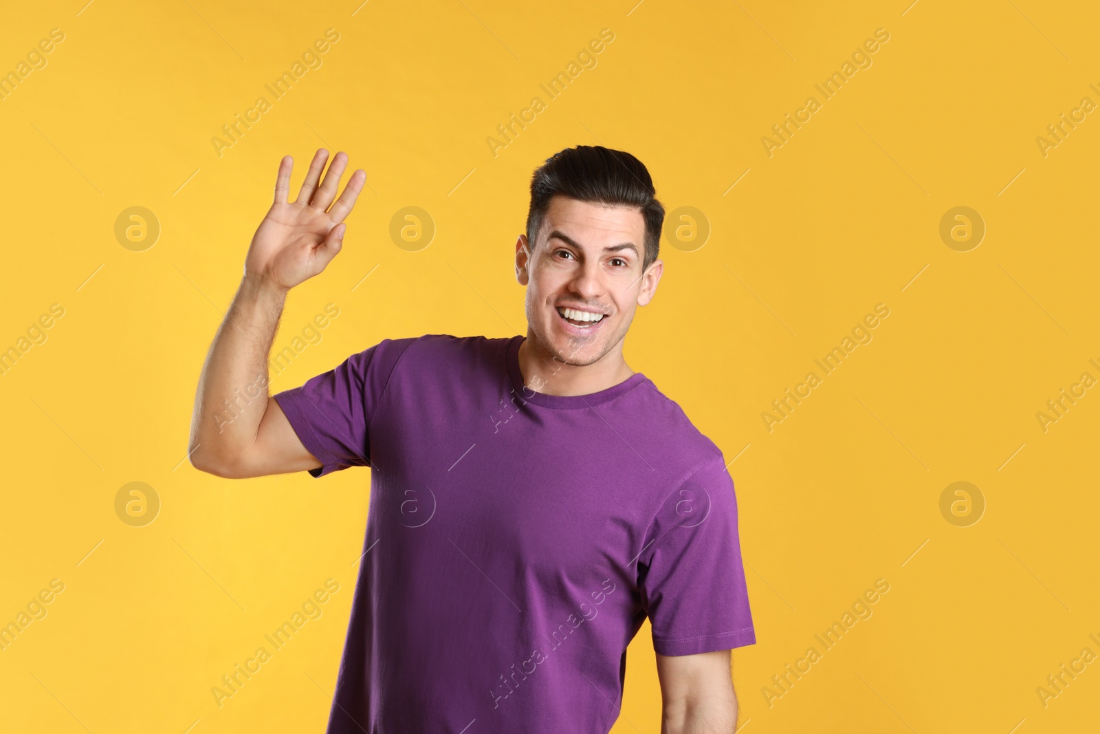 Photo of Cheerful man waving to say hello on yellow  background