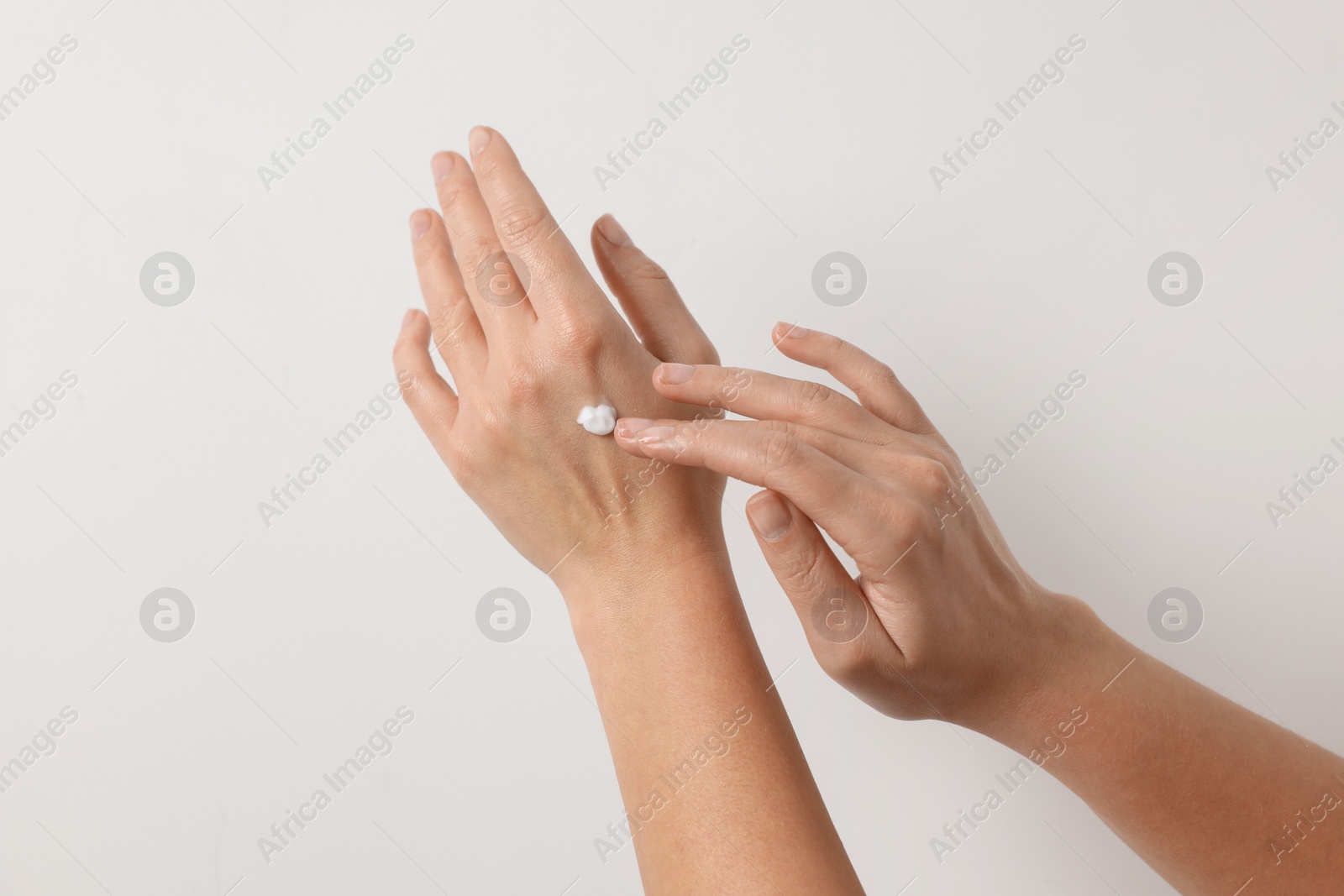 Photo of Woman applying cosmetic cream onto hand on white background, closeup