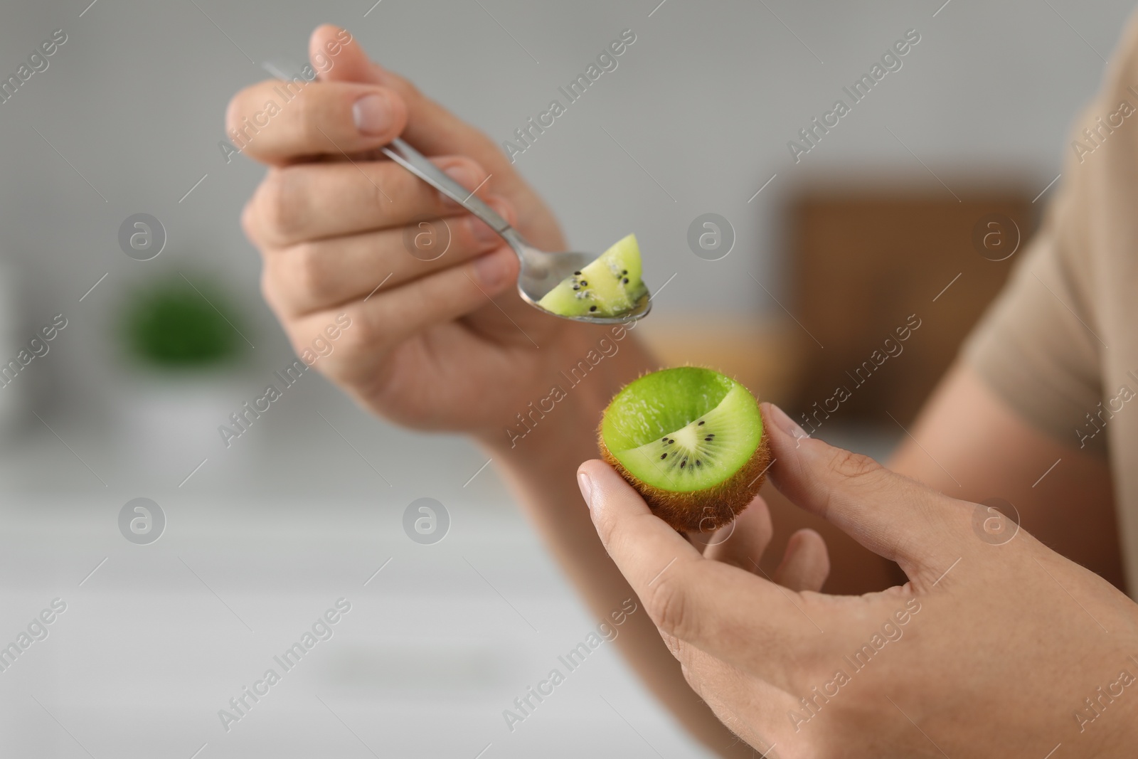 Photo of Man eating kiwi with spoon on blurred background, closeup