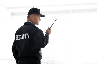 Male security guard using portable radio transmitter on light background