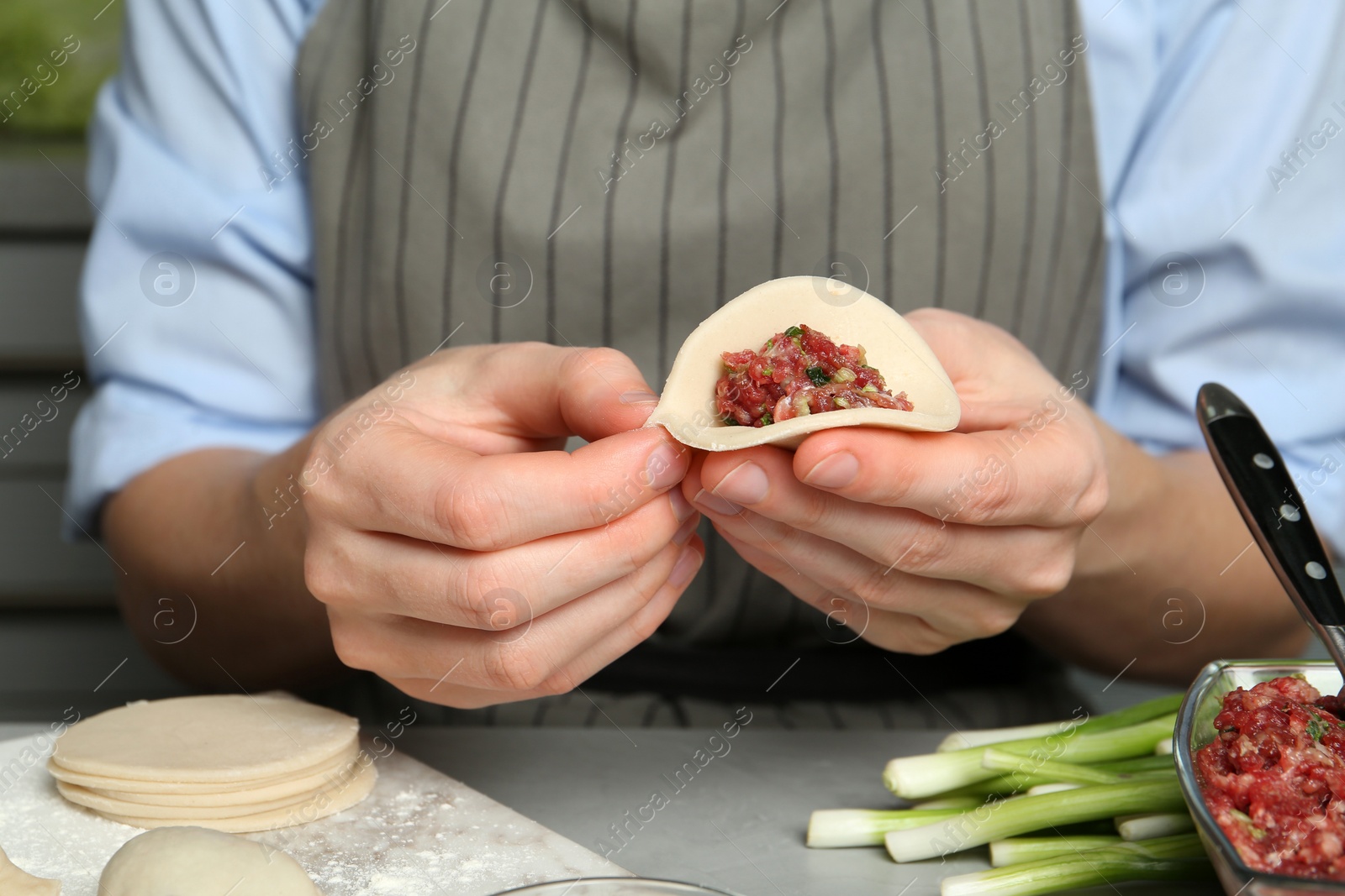 Photo of Woman making gyoza at light grey table, closeup