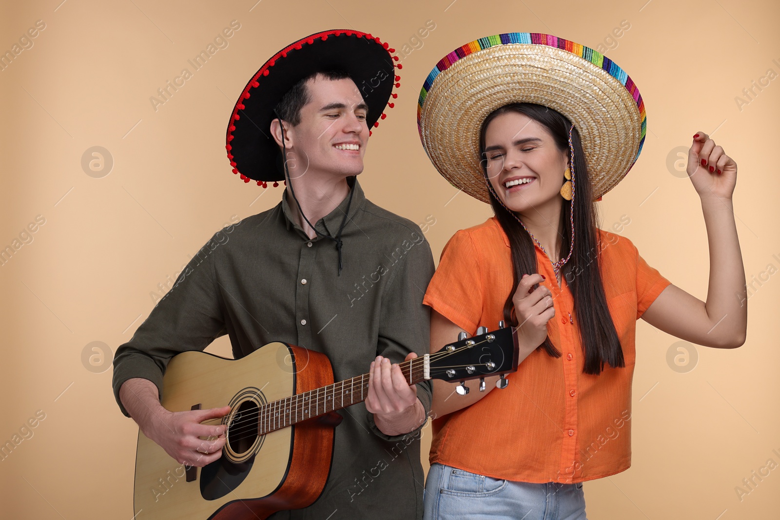 Photo of Lovely couple woman in Mexican sombrero hats playing guitar on beige background