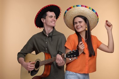 Photo of Lovely couple woman in Mexican sombrero hats playing guitar on beige background