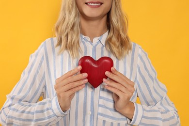 Happy volunteer holding red heart with hands on orange background, closeup