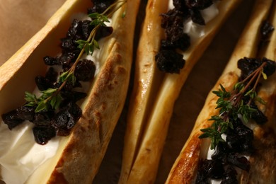 Photo of Tasty baked parsnips with sauce, prunes and thyme on parchment, closeup