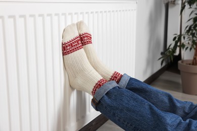 Woman warming legs on heating radiator near white wall, closeup