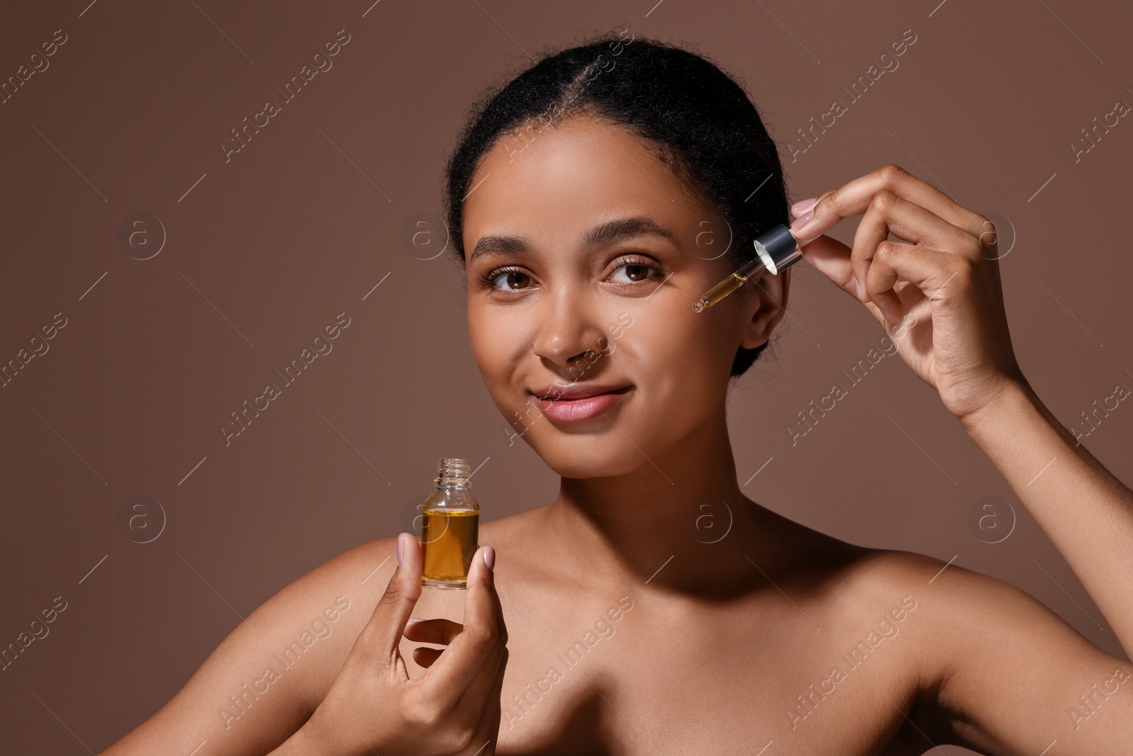 Photo of Beautiful woman applying serum onto her face on brown background