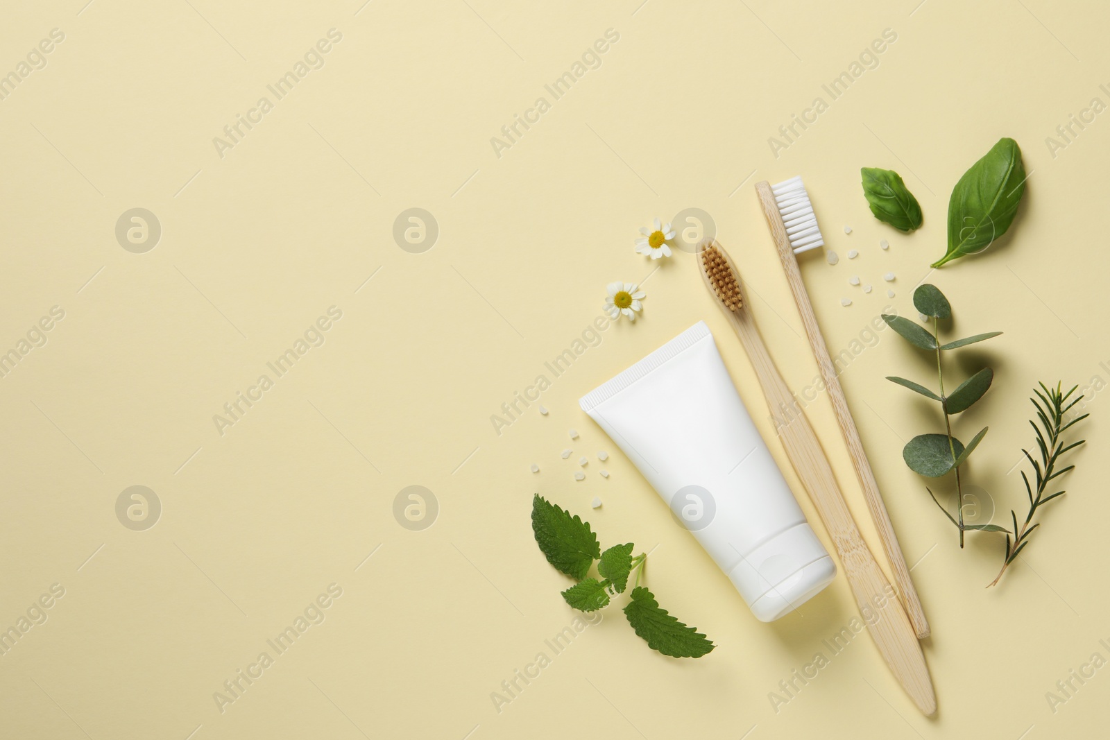 Photo of Flat lay composition with bamboo toothbrushes, tube of cream and herbs on beige background. Space for text