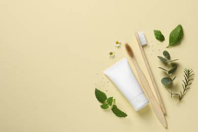 Photo of Flat lay composition with bamboo toothbrushes, tube of cream and herbs on beige background. Space for text
