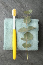 Photo of Plastic toothbrush, eucalyptus branch and towel on grey table, top view