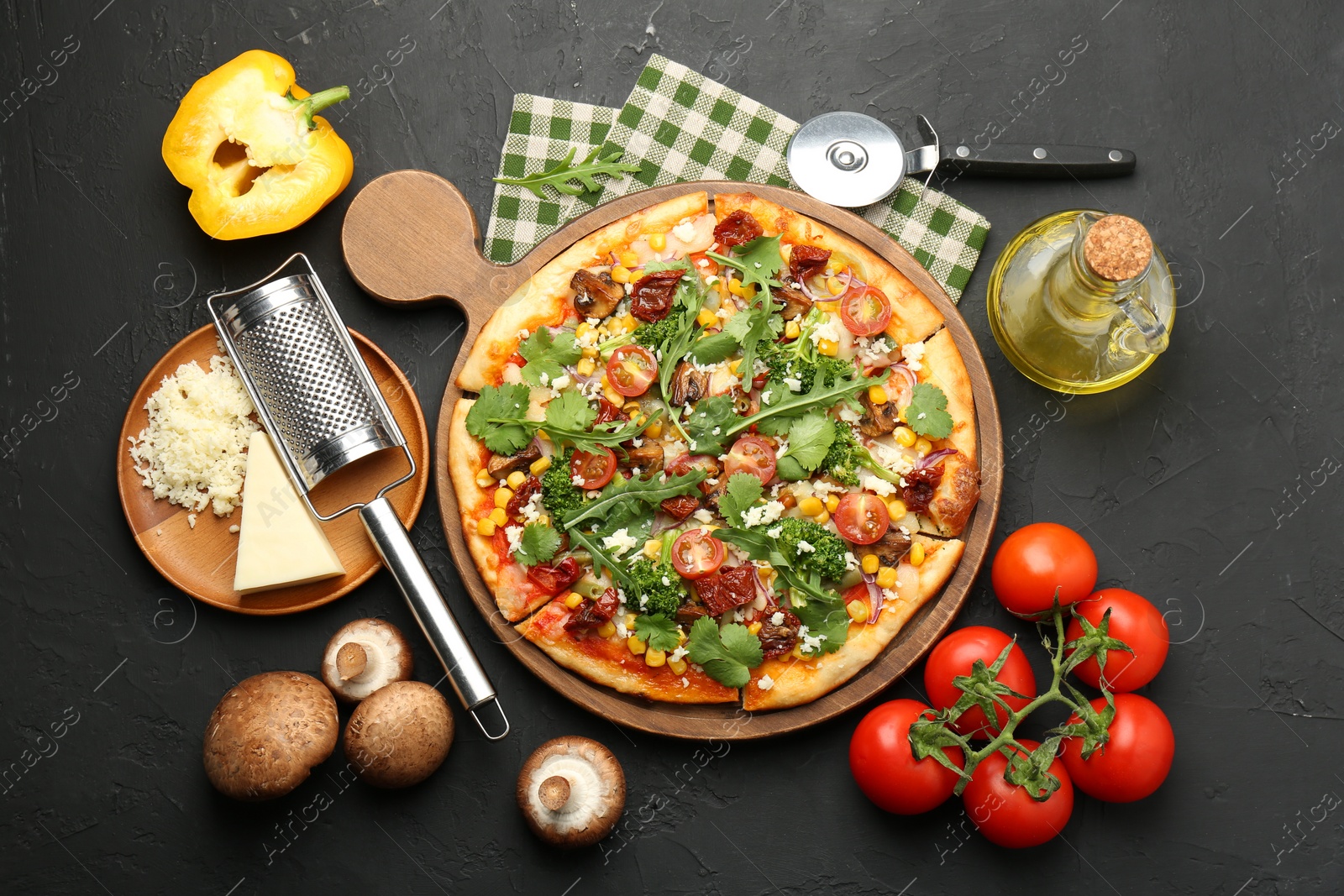 Photo of Delicious vegetarian pizza, ingredients, cutter and grater on black table, flat lay