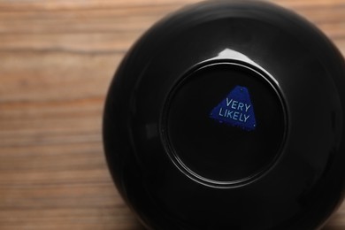 Photo of Magic eight ball with prediction Very Likely on wooden table, closeup