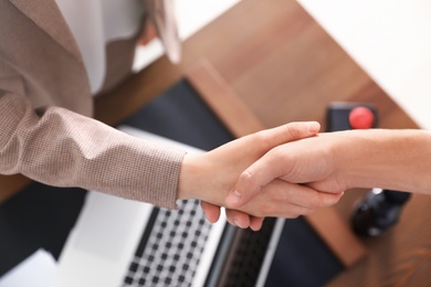 Business partners shaking hands at table after meeting in office, closeup