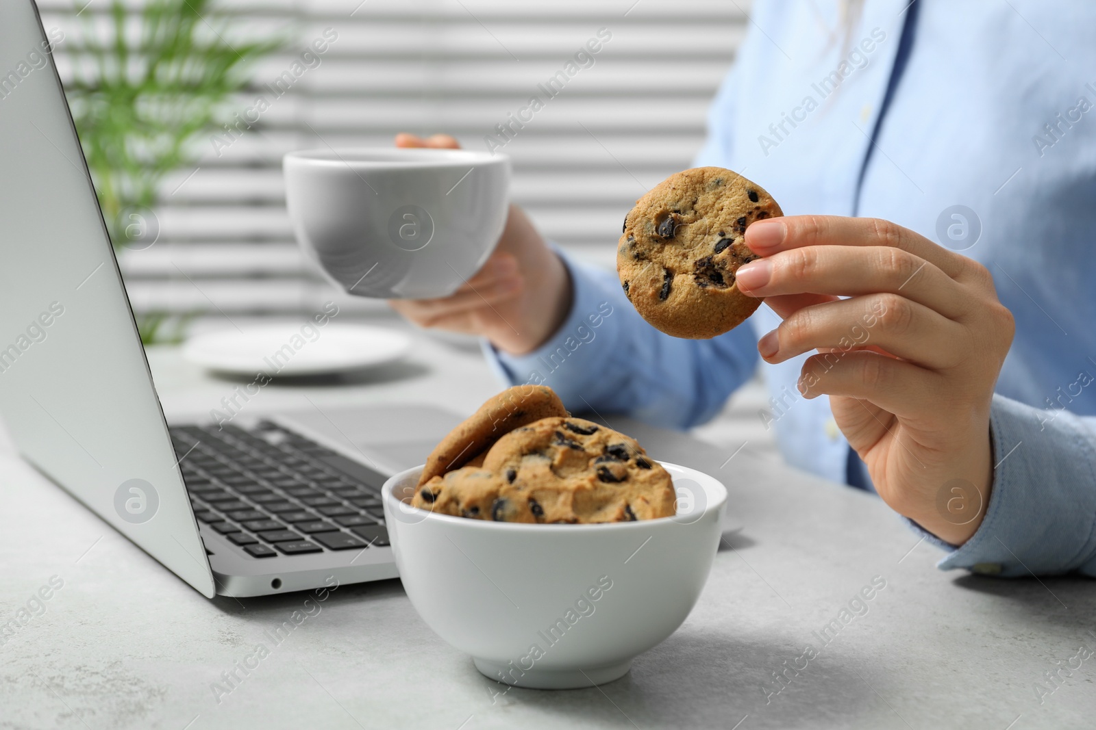 Photo of Office worker with chocolate chip cookie and cup of drink at light gray table indoors, closeup