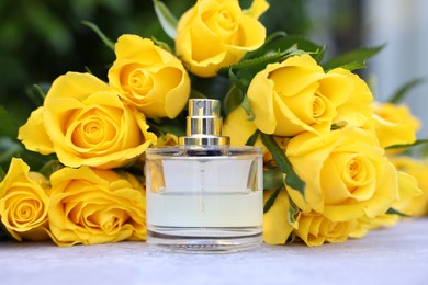 Photo of Perfume and beautiful bouquet of yellow roses on light table, closeup