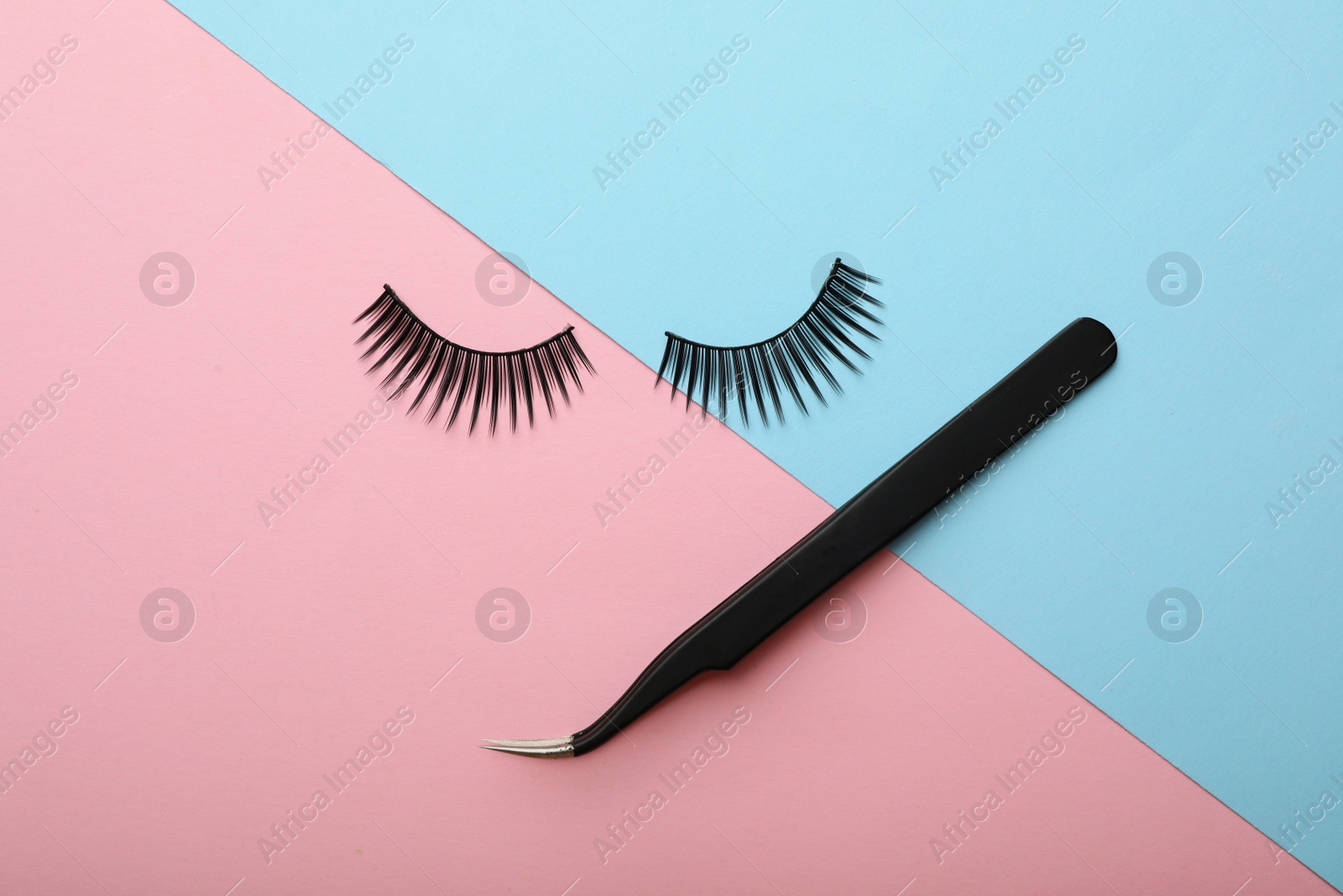 Photo of Artificial eyelashes and tweezers on color background, top view