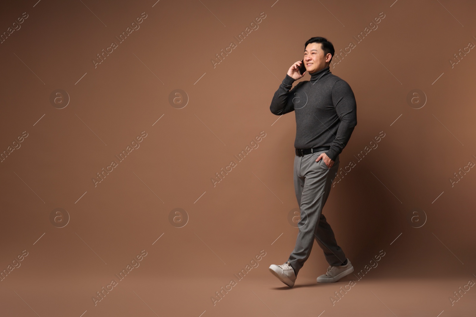 Photo of Full length portrait of happy man talking by smartphone on brown background. Space for text