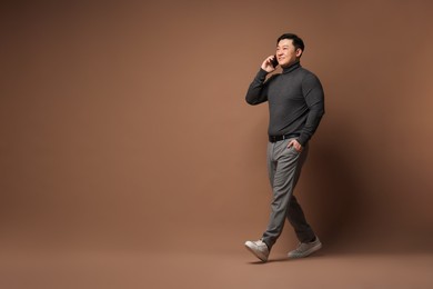 Full length portrait of happy man talking by smartphone on brown background. Space for text