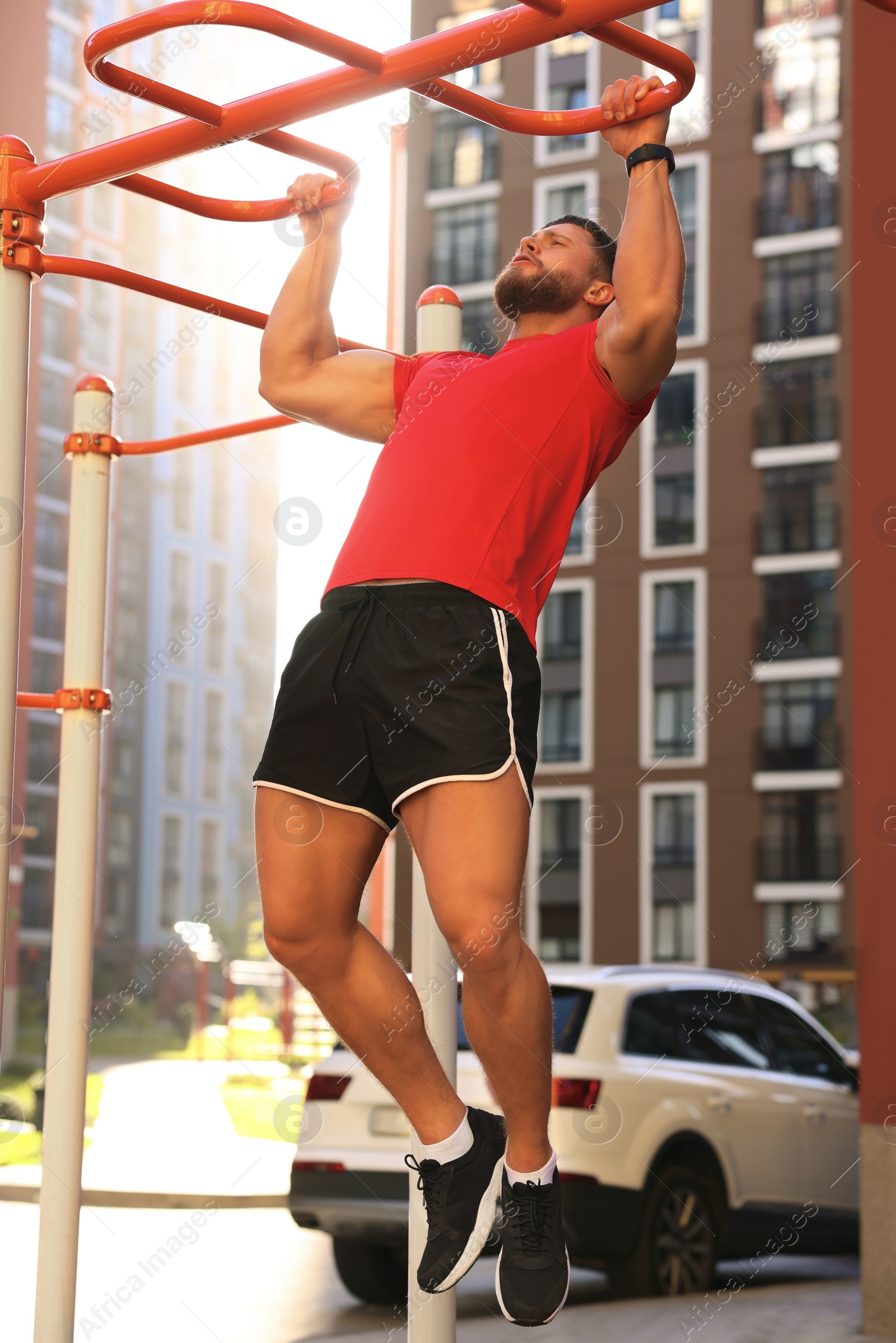 Photo of Man training on horizontal bars at outdoor gym on sunny day