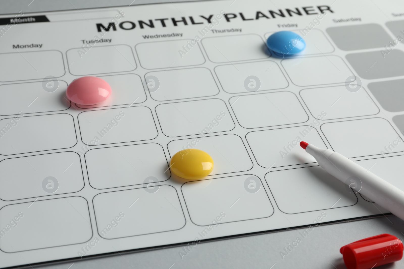 Photo of Timetable. Planner with bright magnets and red felt pen on grey table, closeup