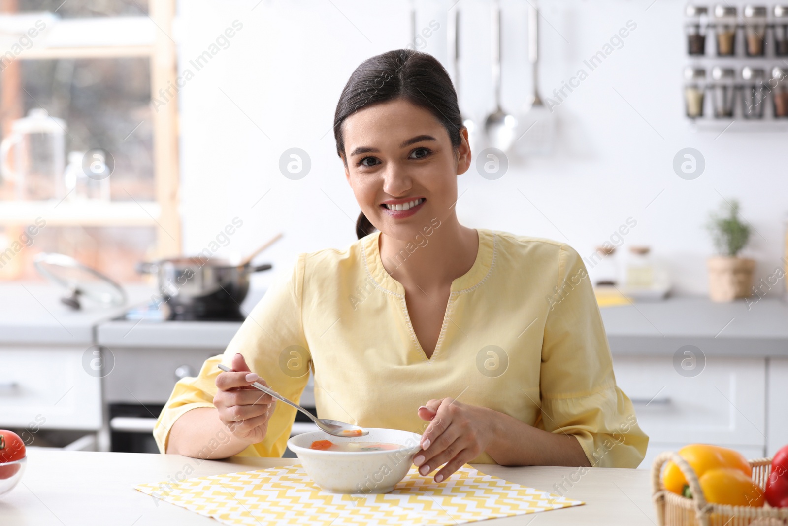 Photo of Young woman eating tasty vegetable soup at table in kitchen